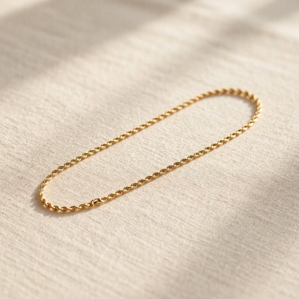 A delicate gold rope chain bracelet laid flat on neutral linen